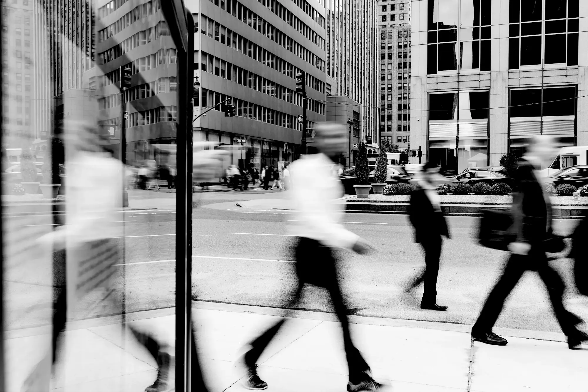 Black and white city street scene with blurred pedestrians walking past office buildings.
